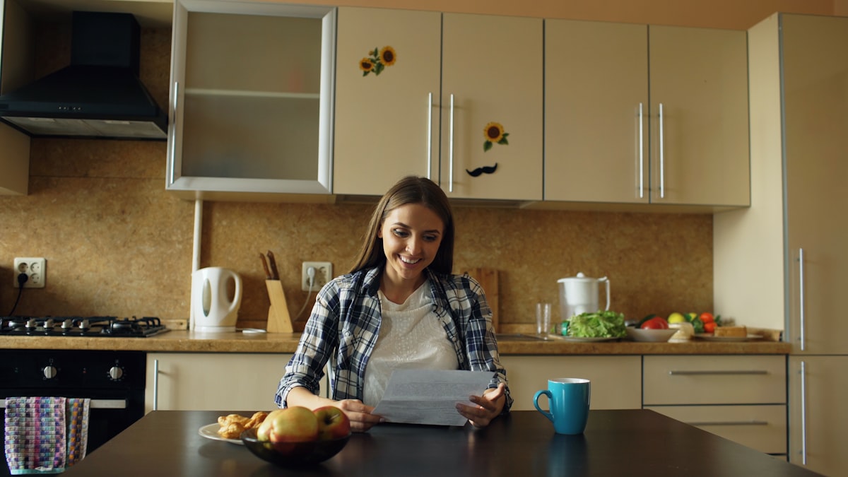 A woman reading a document at her kitchen table in morning light