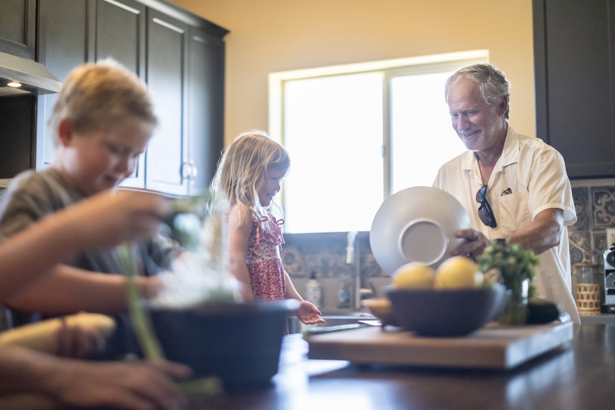 A grandfather and his grandchildren preparing food together in a kitchen